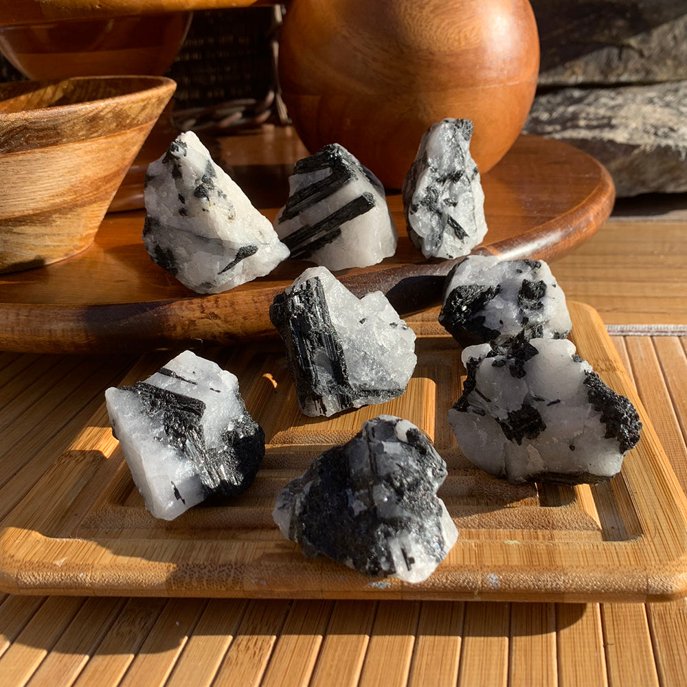 A group of rough tourmalinated quartz pieces on a bamboo tray, each with a different pattern of black tourmaline in white quartz